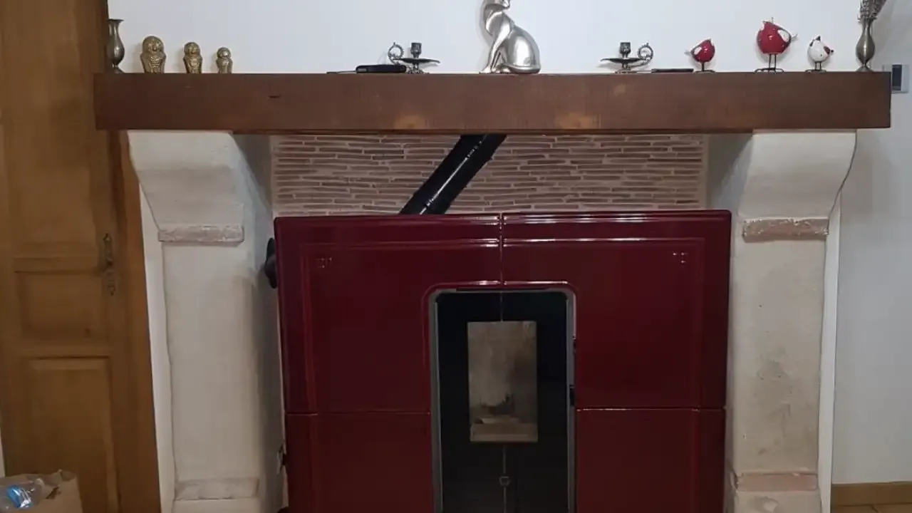 Appareil de chauffage bordeaux inséré dans l’âtre d’une cheminée en brique surmontée d’une poutre en bois